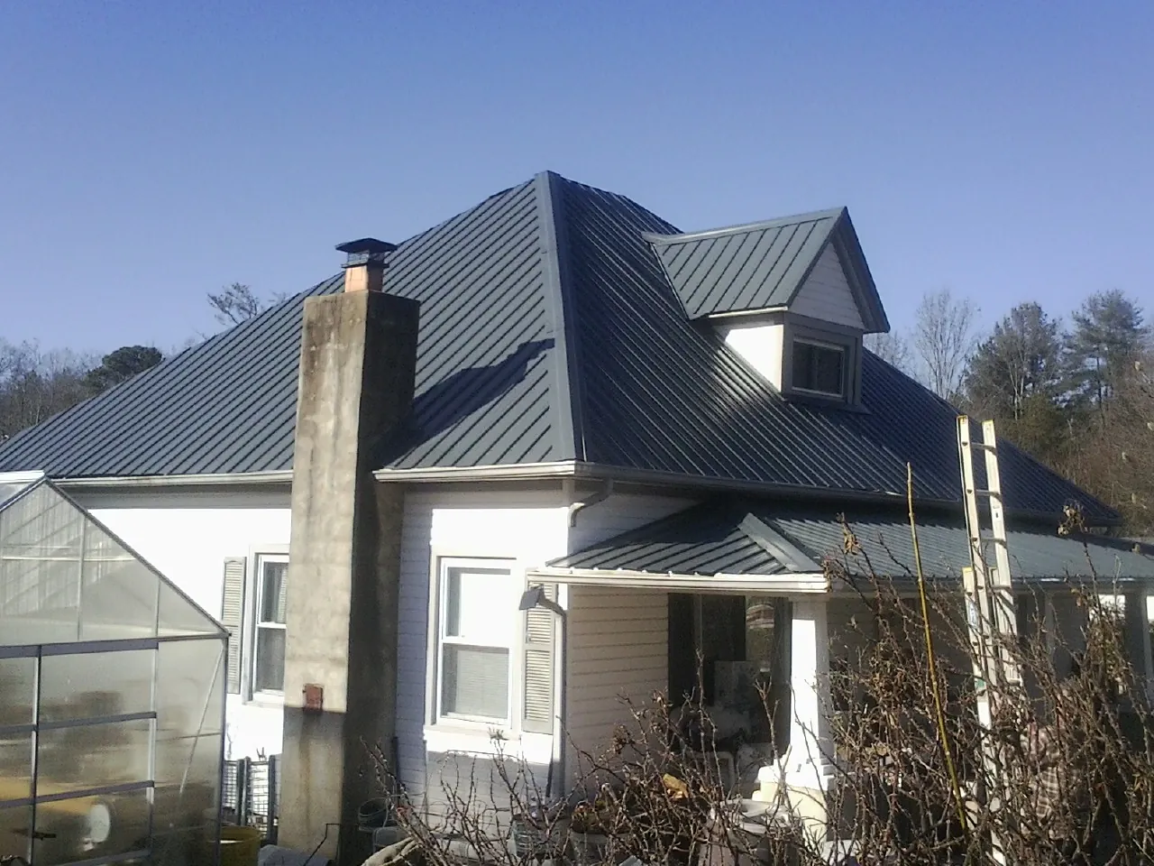 Dark blue standing seam metal roof on a white farmhouse with dormer — Slate & Tile Roof Repair by Roofing Brothers in Ettrick
