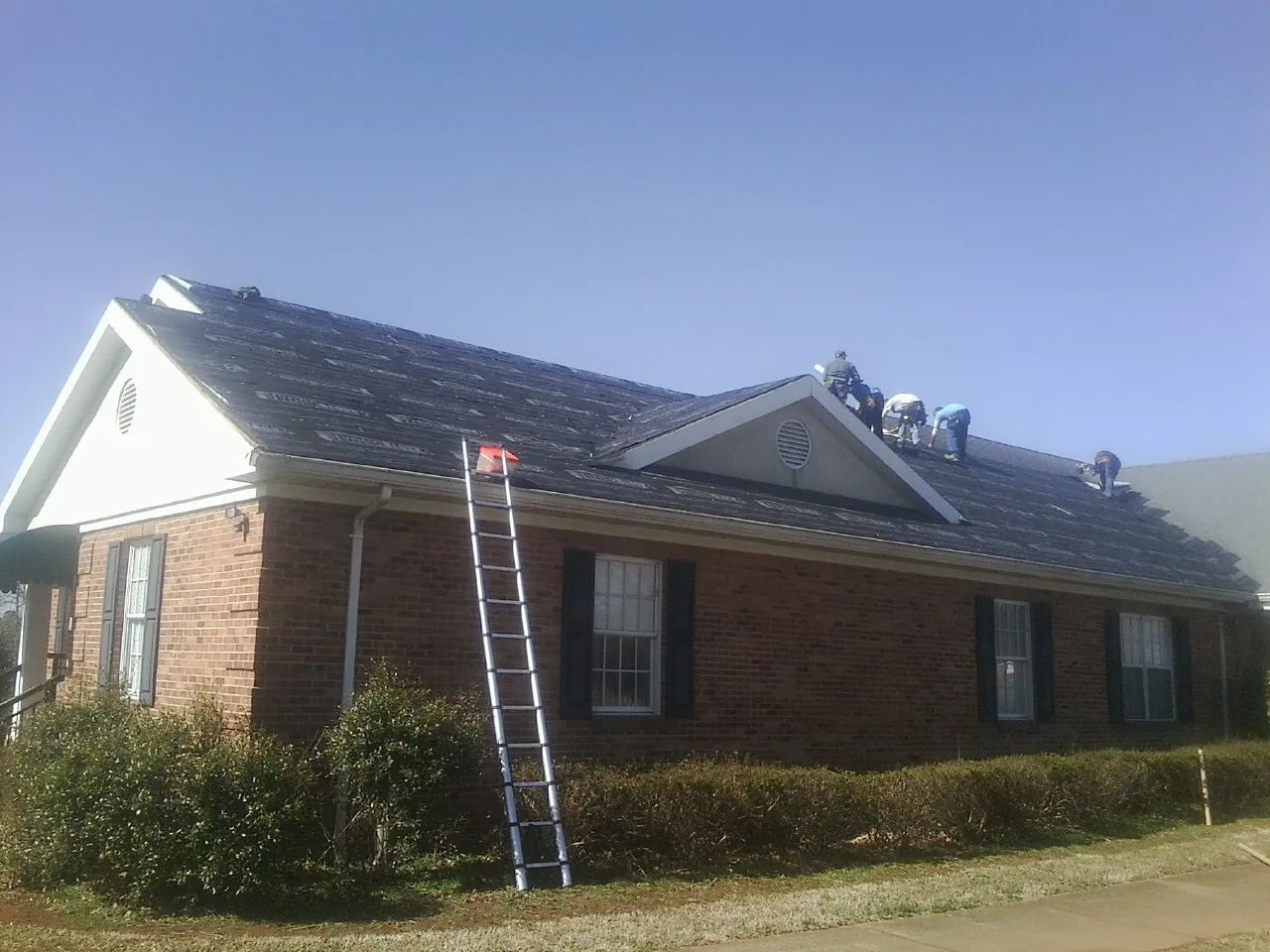 Crew tearing shingles off a brick ranch roof with a ladder set — Metal Roof Repair work by our crew in Ettrick