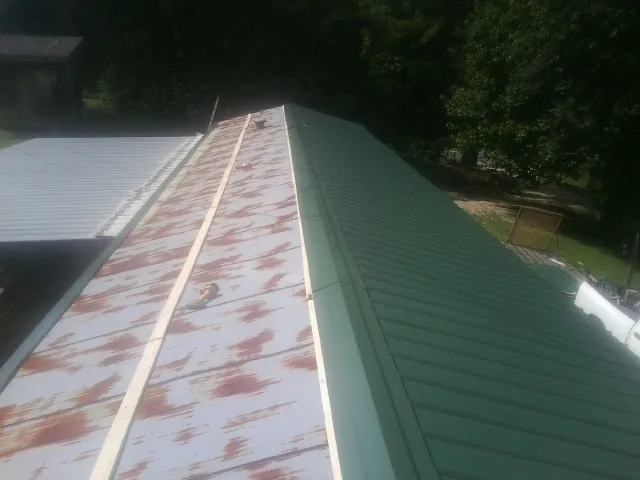 Old rusted panels beside newly installed green metal roofing — Wind Damage Roof Repair by Roofing Brothers in Ettrick