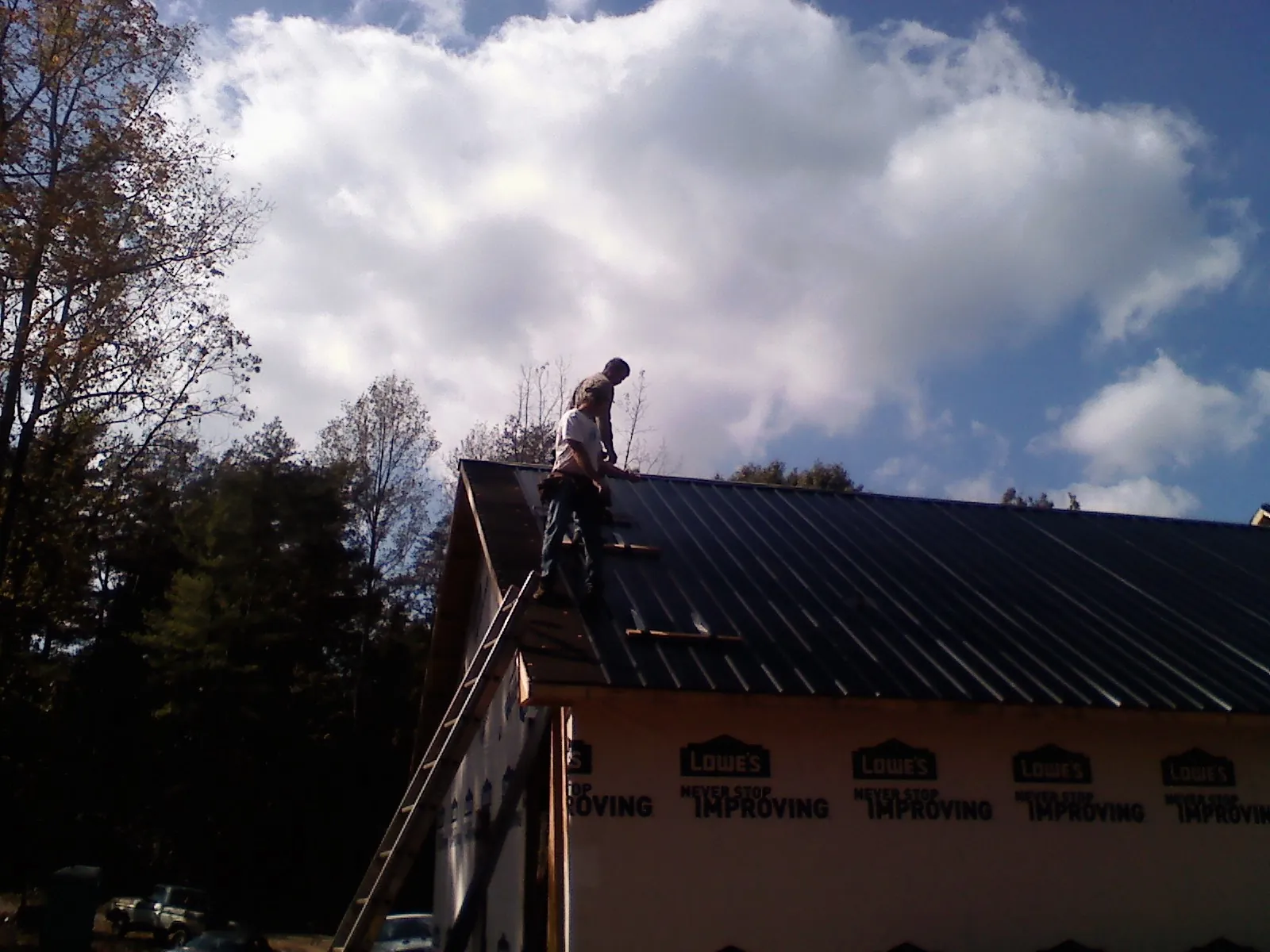 Roofer fastening dark metal panels high against a cloudy sky, from a Roof Inspection job in Ettrick