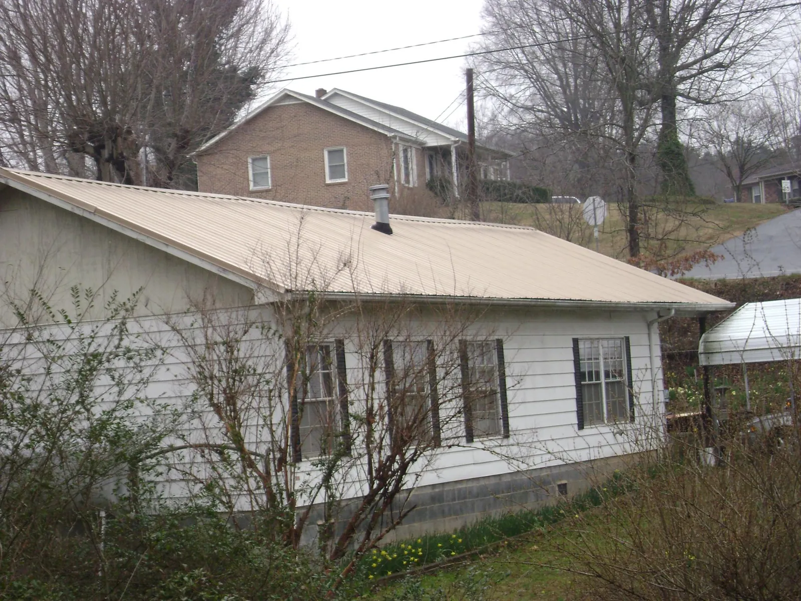 Tan metal roof on a white sided house set into a hillside — Commercial Roofing by Roofing Brothers in Ettrick